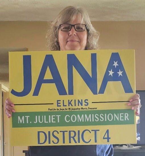 Jana holding her yellow campaign yard sign